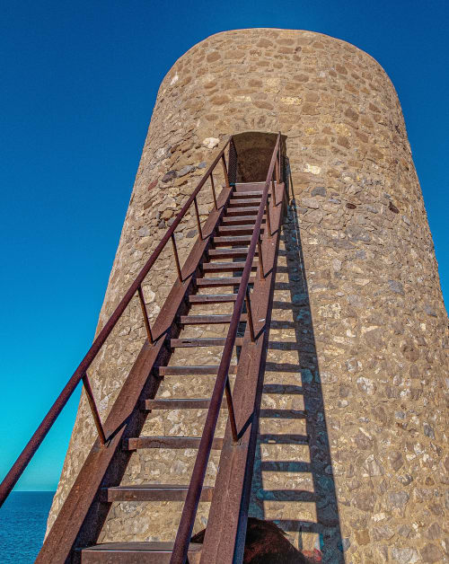 Escaleras oxidadas de metal ascendiendo por torre histórica de piedra con vistas al Mar Mediterráneo, Mojácar