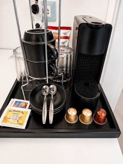 Zona caffè con macchina a capsule, tazza nera, bicchieri, cucchiai e tè Sir Winston presso la guest house B&B Pellicano
