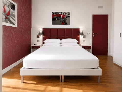 Camera moderna con testata bordeaux, biancheria bianca e pavimento in legno al B&B Pellicano di Reggio Calabria