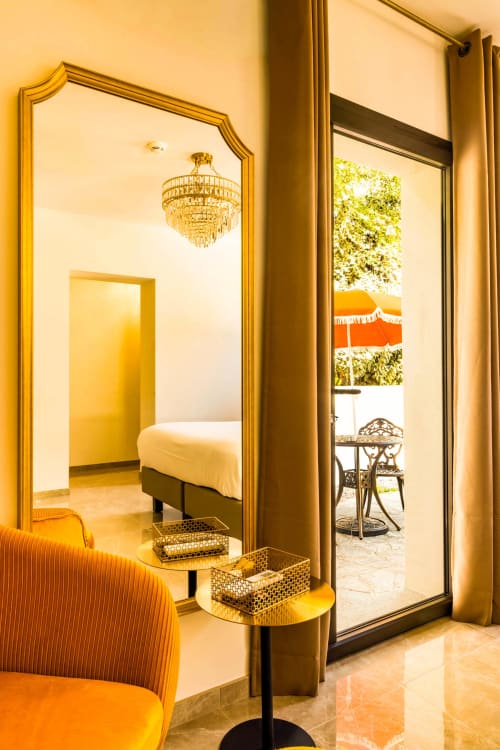 Chambre luxueuse à l'Hôtel Villa Martini à Ajaccio avec détails dorés, mobilier élégant, lustre et vue sur le jardin