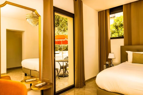 Chambre luxueuse à l'Hôtel Villa Martini d'Ajaccio avec décor doré, lits jumeaux, miroir, lustre, vue sur jardin et terrasse