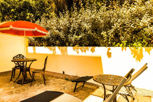 Patio de la chambre jardin de l'Hôtel Villa Martini avec parasol rouge, mobilier et verdure luxuriante à Ajaccio