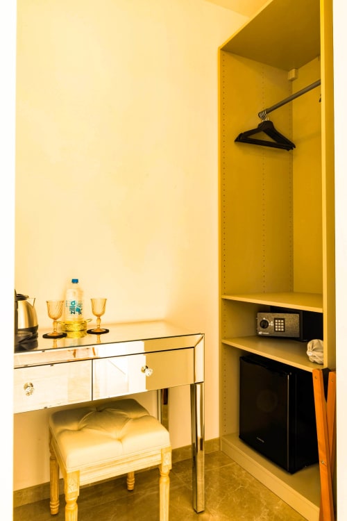 Bright yellow hotel room with mirrored desk, black hanger, safe, and open closet at Hôtel Villa Martini in Ajaccio