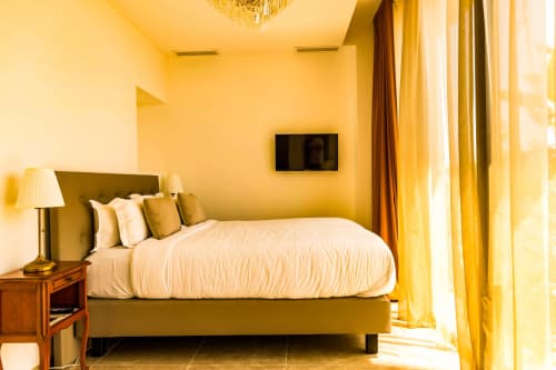 Bright yellow bedroom with olive-green bed, white linens, desk lamp, wall-mounted TV, and golden curtains at Hôtel Villa