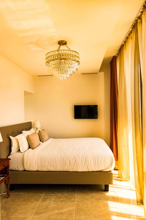 Elegant bedroom at Hôtel Villa Martini in Ajaccio with king bed, crystal chandelier, golden curtains, and flat-screen TV