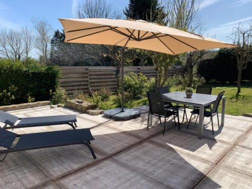 Terrasse extérieure aux Gîtes du Grand Saule à Tardinghen avec table de repas, chaises longues et parasol déporté beige