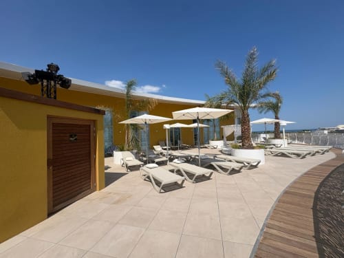 Terrasse ensoleillée d'Agde Luxury Loc avec transats, parasols, palmiers et vue sur mer à Cap d'Agde