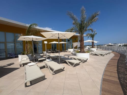 Terrasse ensoleillée d'Agde Luxury Loc avec chaises longues, parasols, palmiers et vue sur la mer