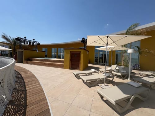 Terrasse sur le toit d'Agde Luxury Loc avec transats, parasols et bâtiment jaune surplombant Le Cap d'Agde