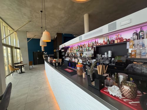 Comptoir de bar moderne chez Vibes Infinity Agde Luxury Loc avec étagères illuminées, bouteilles et design blanc texturé