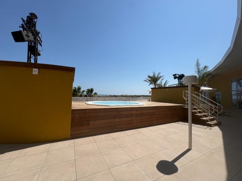 Terrasse sur le toit Agde Luxury Loc avec piscine à débordement, terrasse en bois, bâtiment jaune et vue côtière