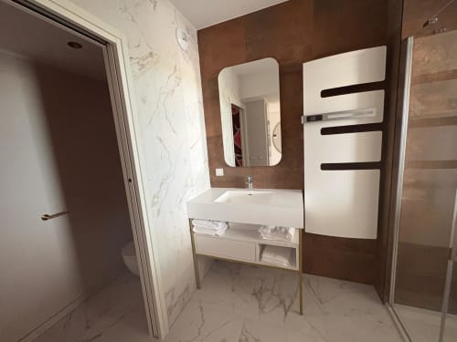 Salle de bain moderne de l'appartement Vibes Infinity avec lavabo blanc, sèche-serviettes chauffant et carrelage effet marbre au Cap d'Agde