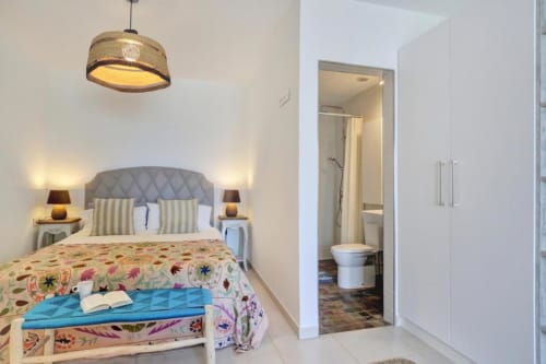 Moderno dormitorio en apartamento de Corralejo con cabecero gris, colcha colorida, lámpara colgante, baño en suite y armario