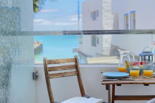 Balcón con vistas al mar en Kamalahouse, Corralejo, con silla de madera, mesa de desayuno, zumo de naranja y edificios costeros