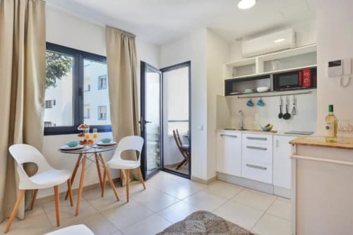 Cocina y comedor modernos en apartamento de Corralejo con vistas al mar, mueblería blanca, encimera de madera y acceso a balcón