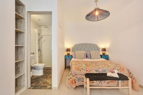 Moderno dormitorio con baño ensuite, apartamento con vistas al mar en Corralejo. Cama con almohadas rayadas, mesillas turquesas