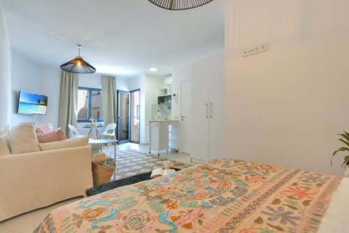 Moderno dormitorio tipo loft en Corralejo con vista al mar, cama, sofá, cocina y acceso a balcón