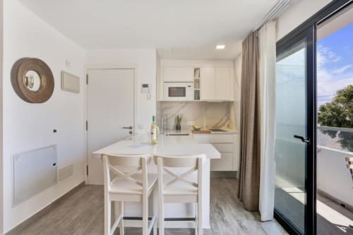 Cocina abierta moderna con comedor y vista al mar en apartamento de Corralejo, muebles blancos y cocineta equipada
