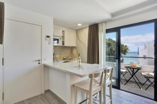Cocina moderna de planta abierta y comedor con vistas al mar en apartamento de Corralejo, con muebles blancos y vista al frente marino