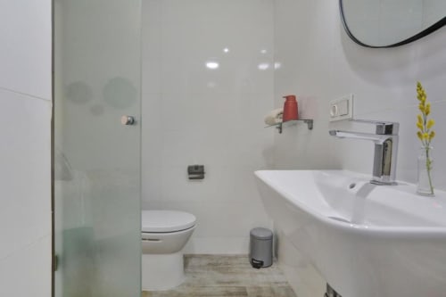 Baño moderno con lavabo blanco, grifo cromado, inodoro y ducha de cristal en el apartamento Kamalahouse SL de Corralejo