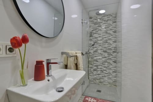 Baño moderno en apartamento de Corralejo con lavabo blanco, tulipanes rojos, ducha tipo lluvia y pared de azulejos mosaico