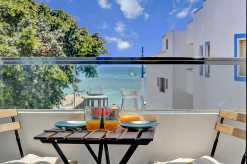Mesa de desayuno en el balcón con vista al mar del apartamento Kamalahouse en Corralejo, con jarra de zumo y platos