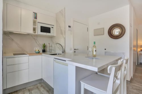 Cocina moderna blanca con backsplash de mármol, isla con asientos y zona de comedor en loft de Corralejo