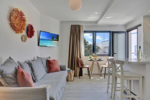 Moderno loft en Corralejo con sofá gris, comedor, vistas al mar por amplios ventanales, TV y arte mural colorido