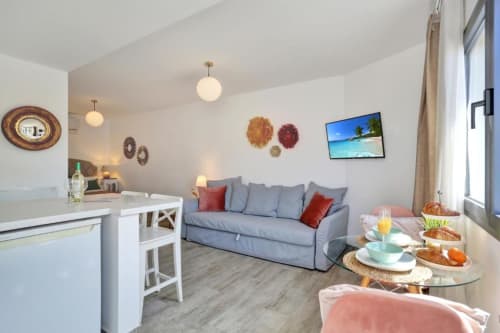 Moderno loft en Corralejo con sofá azul, cocina americana, vista al mar en TV y zona de comedor con desayuno servido