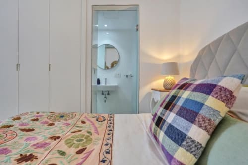 Dormitorio moderno en Kamalahouse, Corralejo, con cabecero acolchado, manta escocesa colorida y baño en suite con espejo