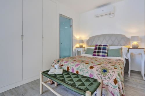 Dormitorio moderno en Corralejo con cabecero acolchado, ropa de cama colorida, puerta turquesa y lámparas gemelas en Kamalahouse