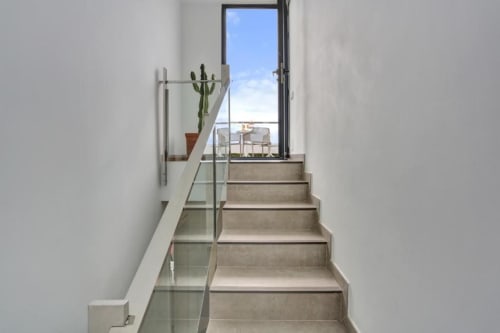 Moderna escalera con barandillas de cristal que conduce a terraza con vistas al mar en el loft Kamalahouse Corralejo