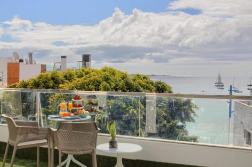 Balcón con vista al mar de Corralejo, tumbonas, mesa de comedor, océano y velerros