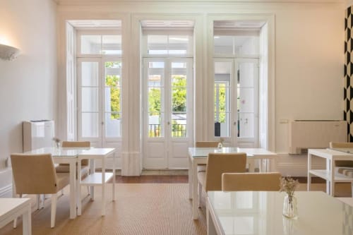 Sala de jantar luminosa na Oporto Comfort Charming House com mesas brancas, cadeiras bege e portas francesas com vista para o Porto