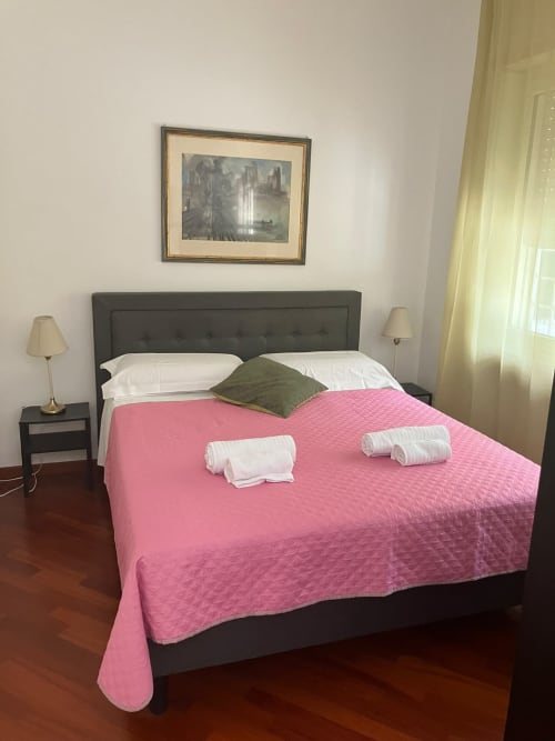 Camera moderna presso Fairome Fleming B, Roma con copriletto trapuntato rosa, testata scura, cuscini bianchi e paesaggio urbano incorniciato