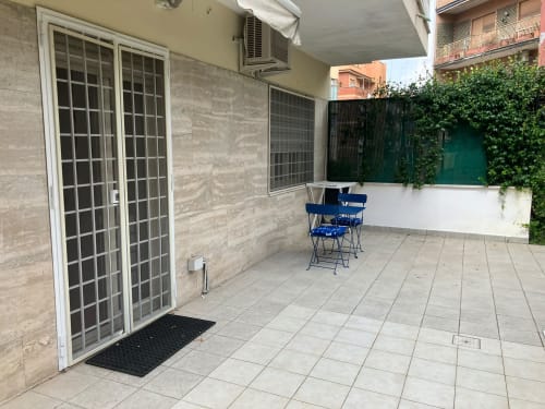 Patio ombreggiato dell'appartamento Fairome Fleming B a Roma con pavimento piastrellato, sedie blu e pareti ricoperte di edera