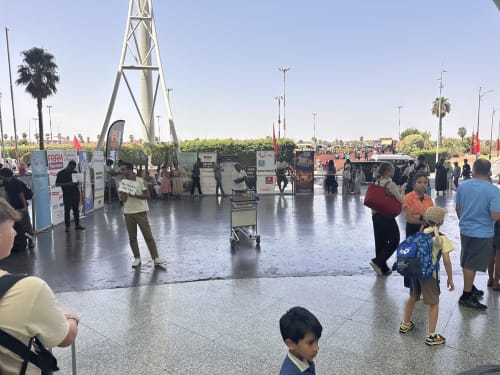 Place publique animée d'Essaouira avec pavés mouillés, tour architecturale, palmiers et visiteurs au Maroc
