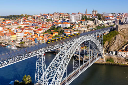 Ponte Dom Luís atravessando o Rio Douro com a paisagem histórica do Porto e edifícios de telhados vermelhos ao fundo.