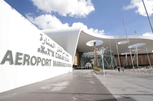 Entrée du terminal de l'aéroport de Marrakech avec architecture blanche moderne et signalétique sous un ciel bleu
