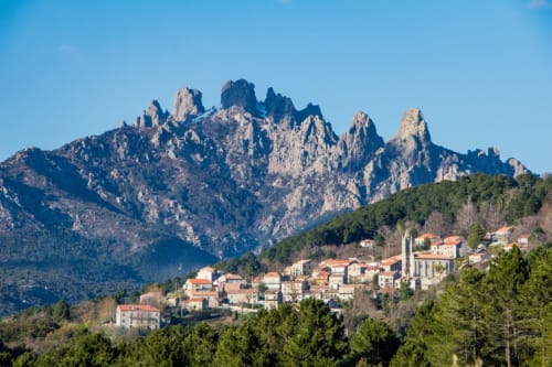 Villa Abbracciu in Pietrosella with dramatic rocky peaks and pine forest backdrop under clear blue sky
