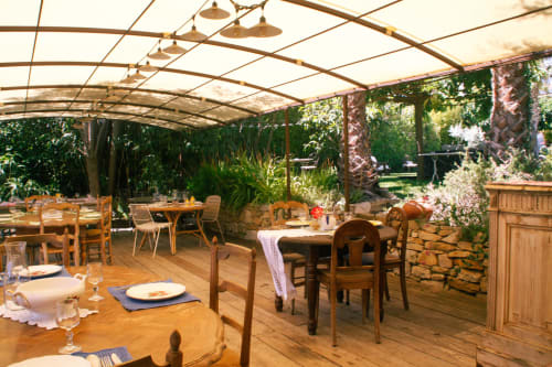 Élégante terrasse couverte du Clos BB à Saint-Cyr sur Mer, avec tables en bois, vue sur le jardin luxuriant et éclairage ambiant
