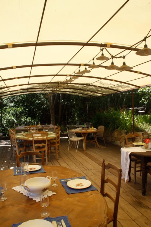 Salle à manger du Clos Bb à Saint-Cyr sur Mer avec tables en bois, couverts dressés et terrasse couverte sous voile crème