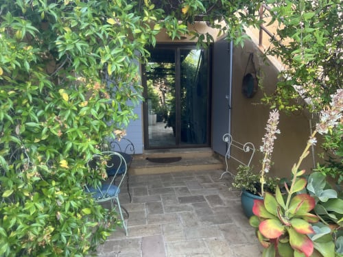 Ingresso della corte lussureggiante del Clos Bb B&B a Saint-Cyr sur Mer con viti rampicanti, piante grasse in vaso e vetro scuro