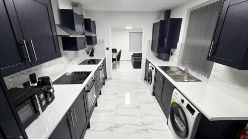 Modern kitchen in Stafford cottage with black cabinets, white marble countertops, stainless steel appliances, and washing