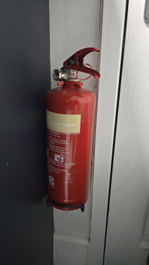 Red fire extinguisher mounted on white wall at Entrepreneur Stays cottage in Stafford