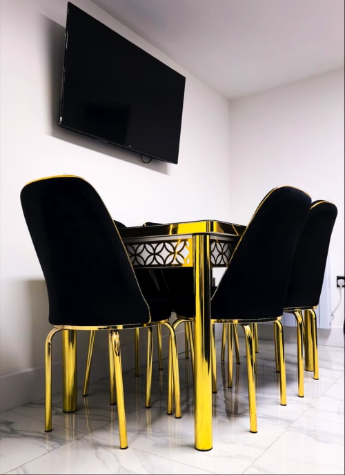 Modern dining area with black velvet chairs, gold-trimmed table, and wall-mounted TV at Entrepreneur Stays cottage in