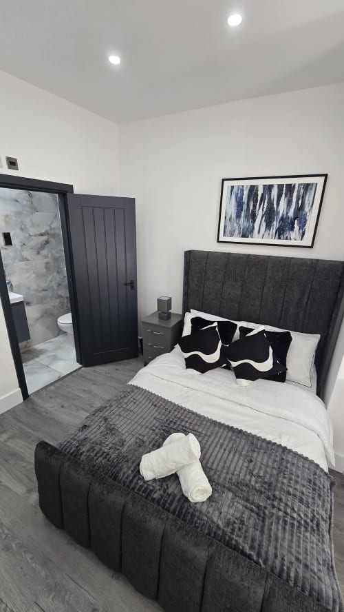 Modern bedroom at Entrepreneur Stays cottage in Stafford with dark headboard, white bedding, black pillows, en-suite
