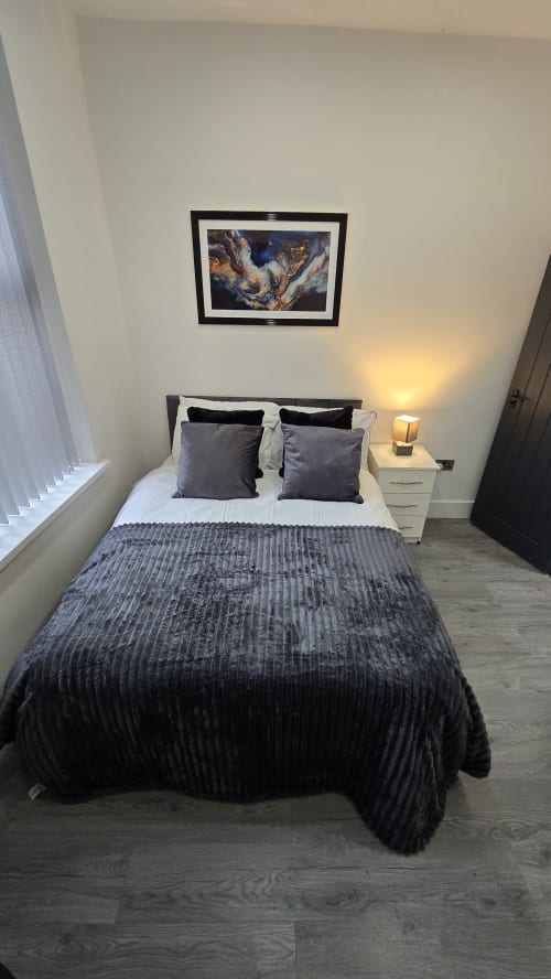 Modern bedroom in Stafford cottage with queen bed, grey bedding, dark pillows, framed artwork, bedside lamp, and window with