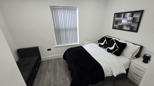 Modern bedroom in Stafford cottage with queen bed, black and white bedding, white nightstand, and vertical blinds