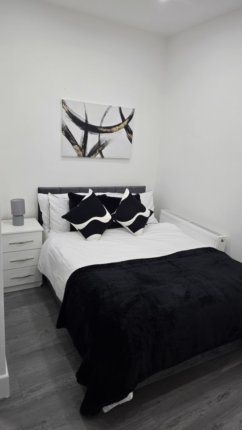 Modern bedroom at Entrepreneur Stays Stafford cottage with black and white bedding, dark wooden floors, and abstract wall art